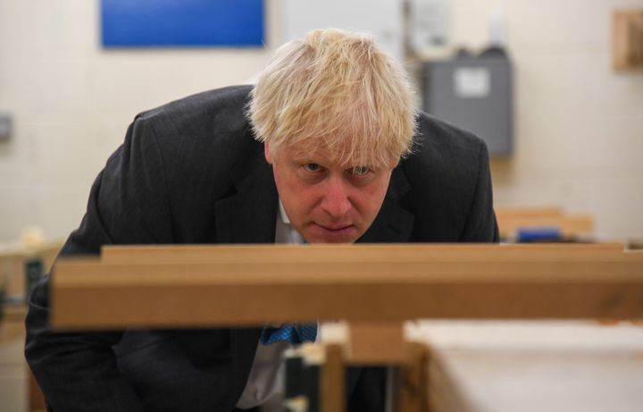 Boris Johnson looks at a piece of wood in a vice during a visit to Exeter College.