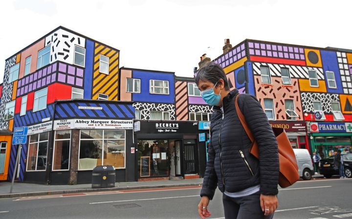 A woman wearing a face mask walks past shops and a mural created by artist Camille Walala, amid the spread of the coronavirus disease (COVID-19), in Leyton, London, Britain, September 29, 2020. REUTERS/Peter Cziborra