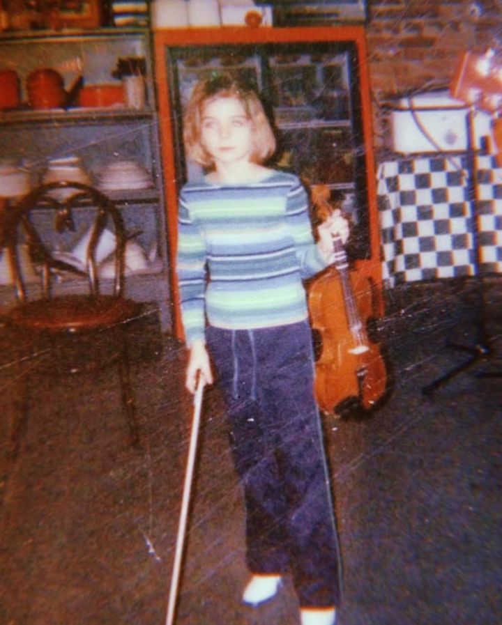 The author holding their fiddle at a restaurant in the early 2000s. They've always played bluegrass music, being from the South, and can still saw a pretty good "Road to Columbus." Restaurants in rural areas of the South often have jam nights; this was probably one of them.