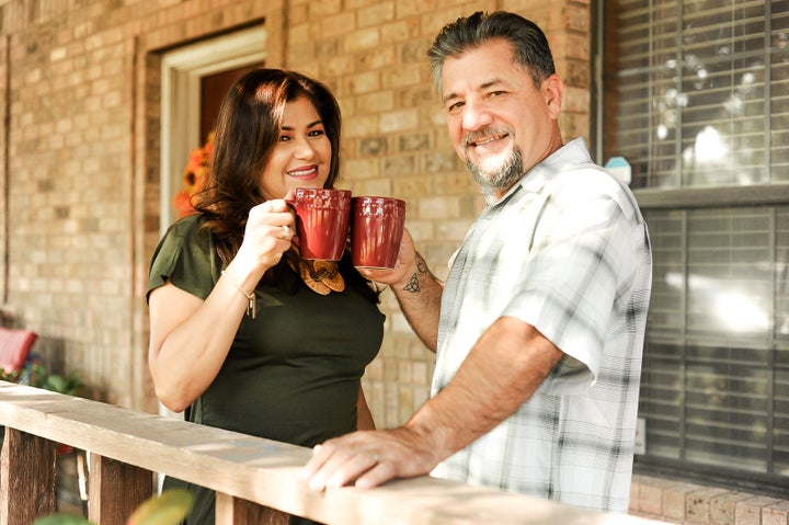 The couple cheers with coffee mugs outside their home. 