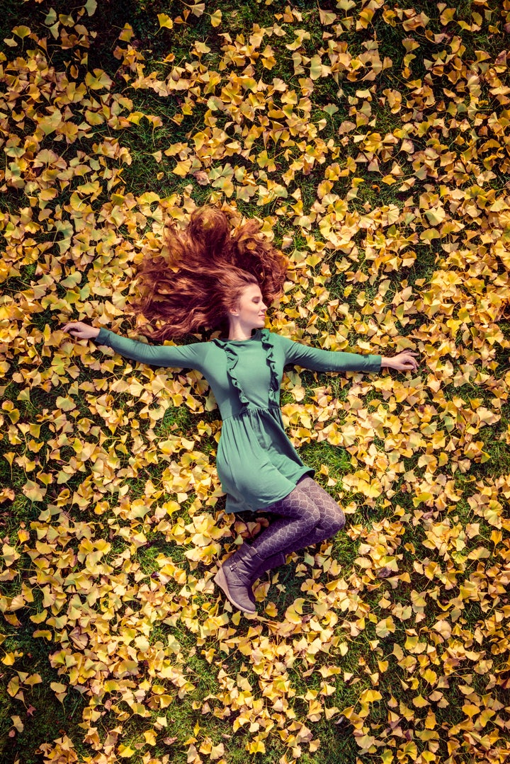 A beautiful woman with red hair in a green dress lies in the autumnal foliage of a ginkgo tree. Copy space for design.