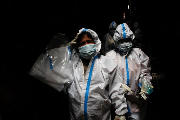 A health worker in personal protective equipment reacts as she and the rest of the team walk through...