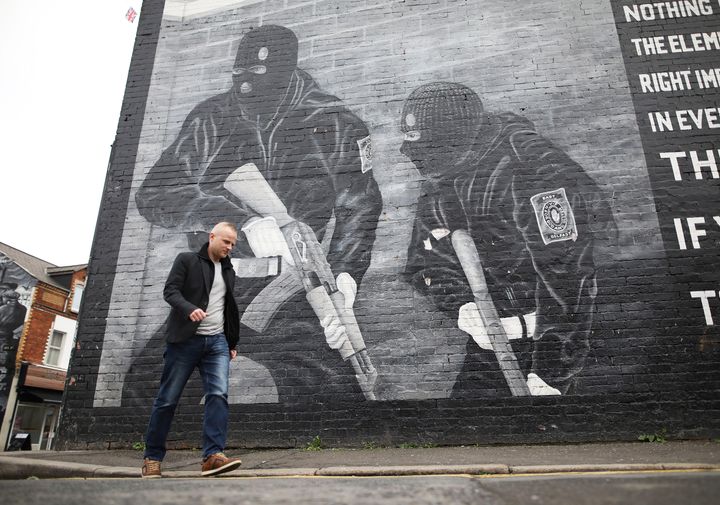 Loyalist activist Jamie Bryson walks past a loyalist Ulster Volunteer Force mural in east Belfast, Northern Ireland, in 2019
