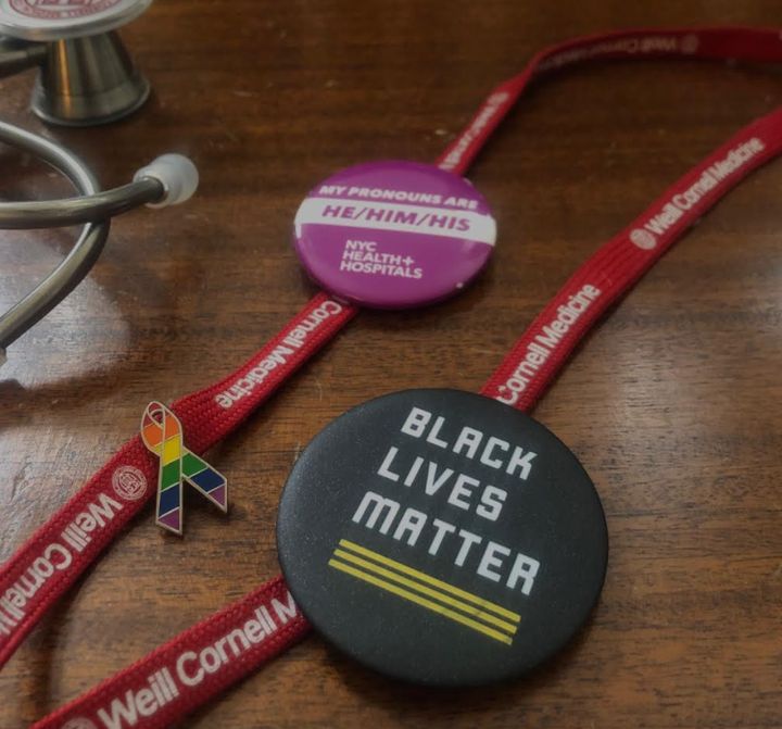 A close-up of the author's rainbow, Black Lives Matter and pronoun pins.