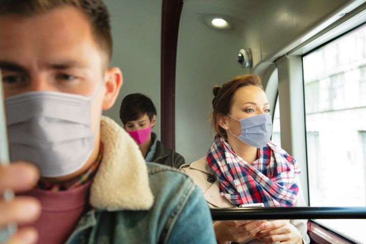 Three young people wearing masks and social distancing during a bus ride, looking serious.