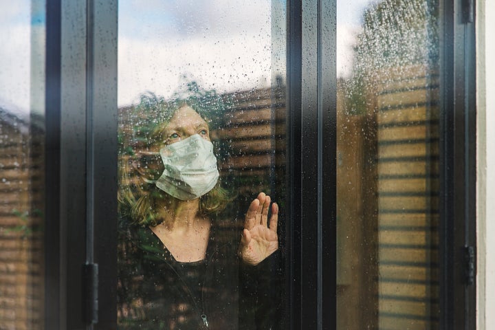 Senior woman with mask looking through window