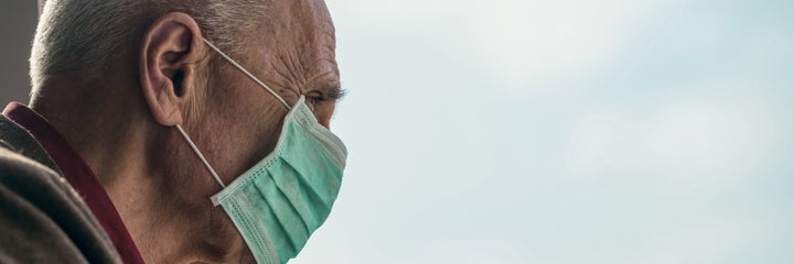 old man wearing medical face mask looking through window blue sky background healthcare concept