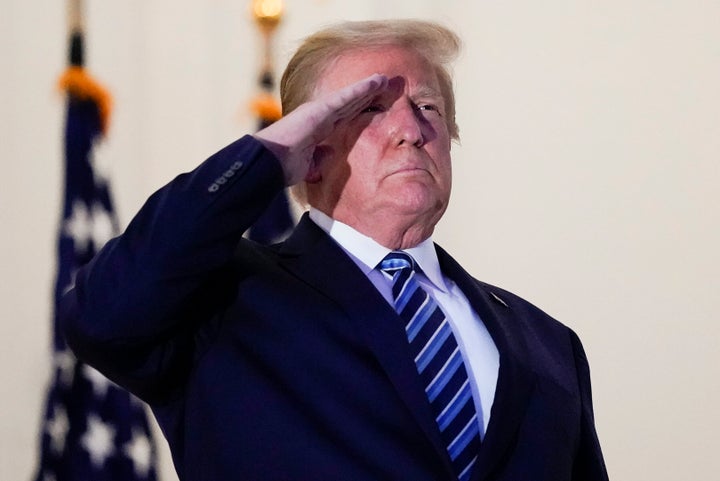 President Donald Trump salutes from a White House balcony on Monday after returning from Walter Reed National Military Medical Center.