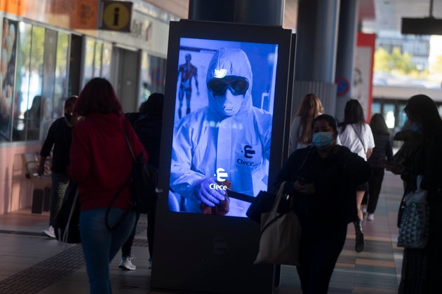 People pass by a poster thanking medical workers at a bus station in Madrid, Spain, Wednesday, Oct. 7, 2020. About 5.2 million people in Spain, including nearly 4.8 million residents in or around Madrid, are under restrictions on movement due to the second wave of the coronavirus pandemic. (AP Photo/Paul White)