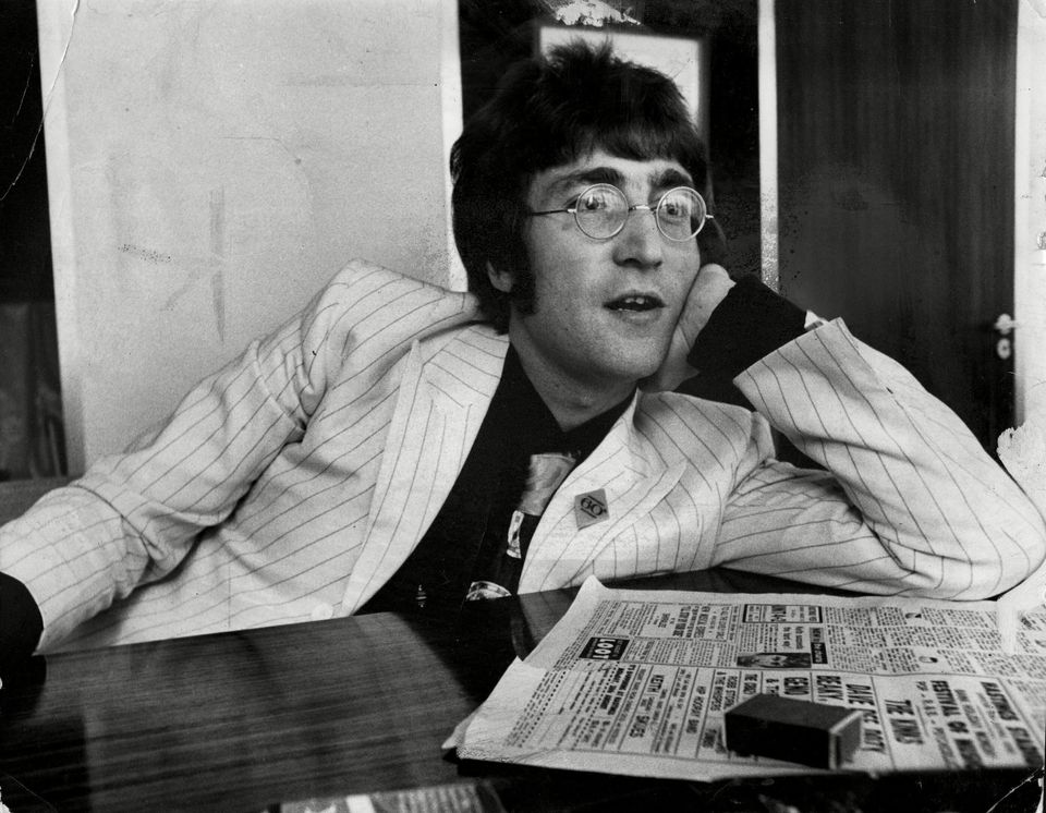 John Lennon Musician And Member Of The Beatles Leaning On A Table.