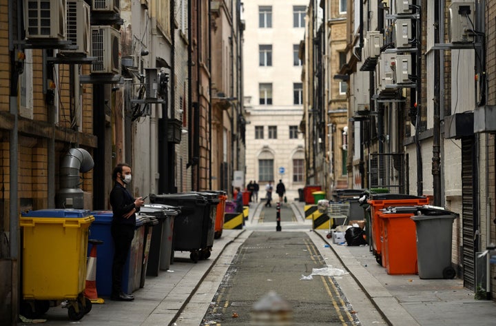 A man wearing a face mask or covering due to the COVID-19 pandemic, stands amongst commercial rubbish bins in Liverpool, north west England.