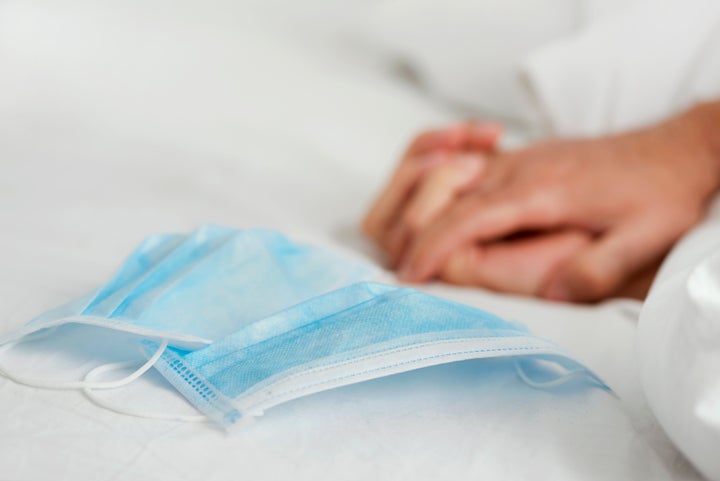 A pair of surgical masks on a bed with two people gripping their hands in the background.