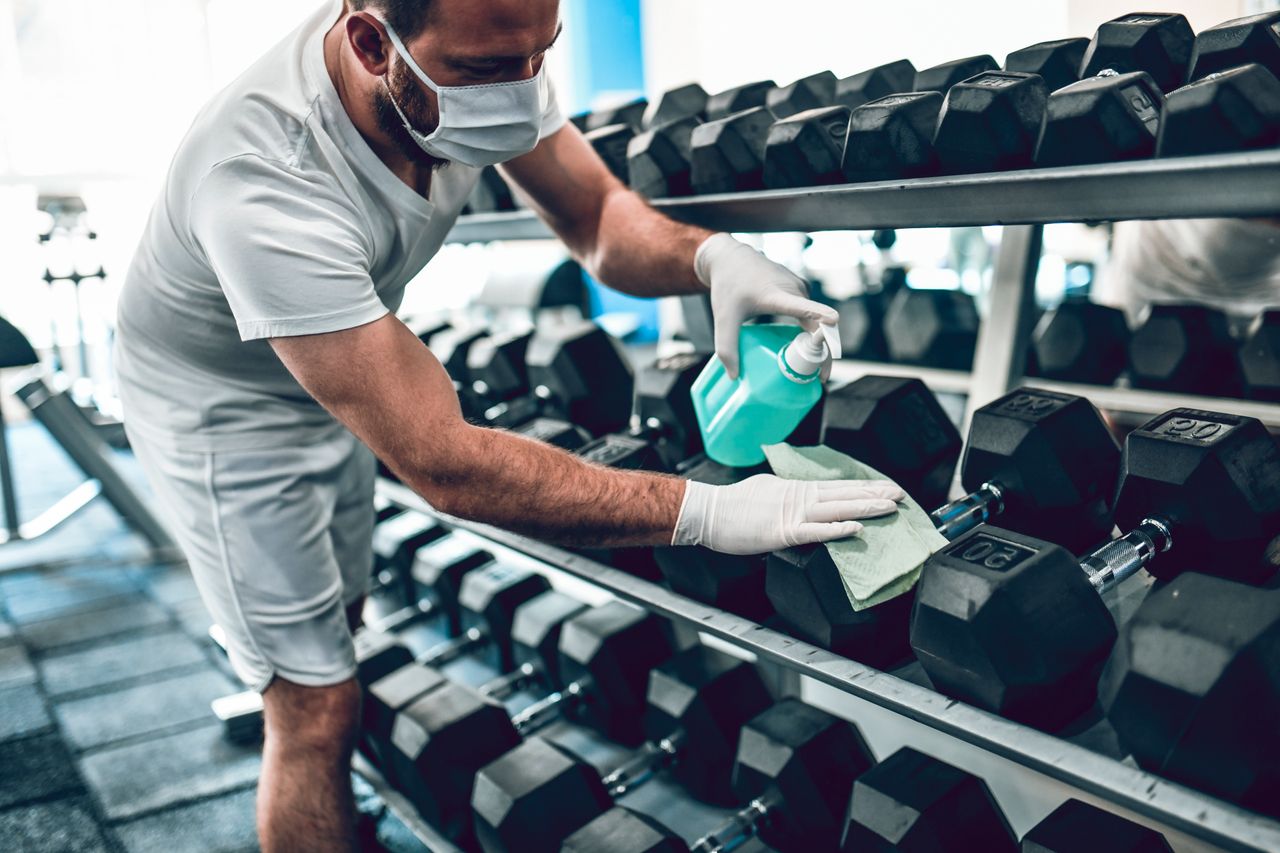 Man wearing a face mask disinfects gym equipment 