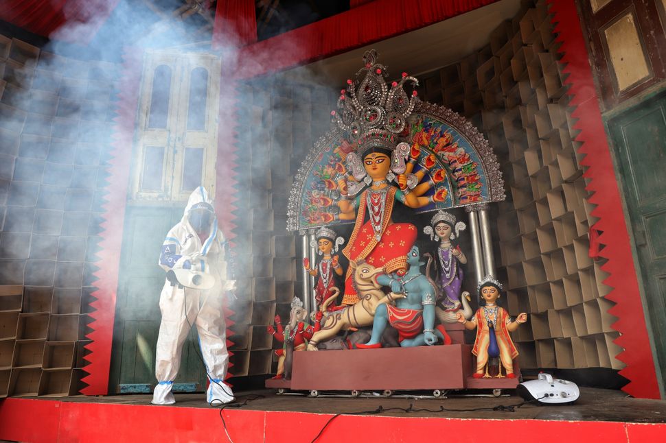 KOLKATA, WEST BENGAL, INDIA - 2020/10/13: A member of the Durga Puja committee dressed in a protective suit sprays disinfectants to sanitise a Pandal in front of an idol of Goddess Durga as a preventive measure against the spread of Coronavirus (COVID-19). (Photo by Jit Chattopadhyay/SOPA Images/LightRocket via Getty Images)