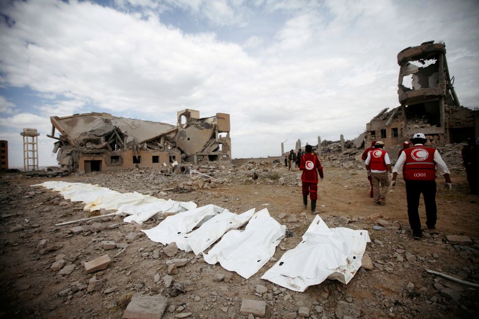 Red Crescent medics walk next to bags containing the bodies of victims of Saudi-linked airstrikes on a Houthi detention cente