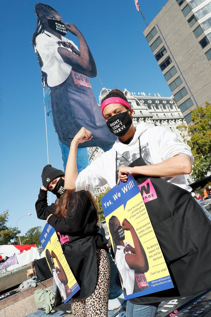 One Fair Wage team members Breanne Delgado (left) and Nikki Cole (right) rally at the base of an 18-foot wooden statue of Elena the Essential, representing service worker’s demand for respect, full pay and fair elections as part of the protests on Saturday.