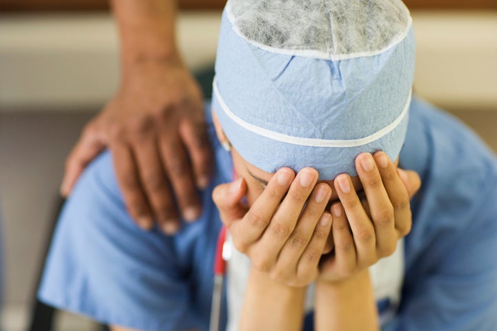 A health-care worker holds her head in her hands in this undated stock photo. A new survey suggests Canadians are less upbeat these days than their U.S. counterparts.