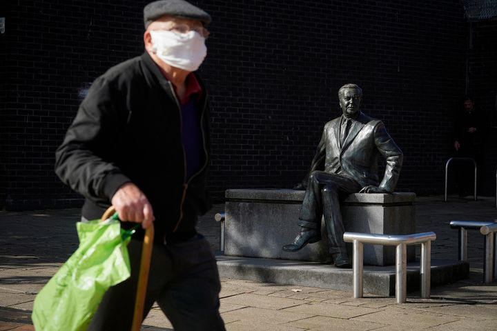 A man wearing a protective face mask walks past a statue of former prime minister Harold Wilson in Huyton in Liverpool.