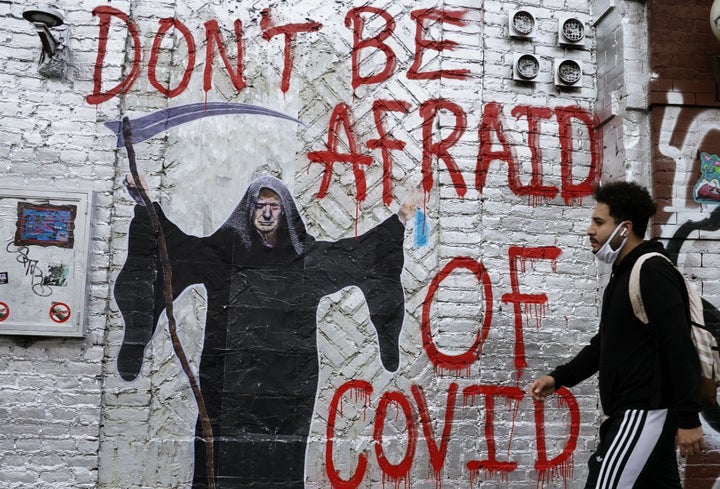 A man walks past a mural by the artist who goes by the name "Pure Genius" depicting President Donald Trump as the Grim Reaper