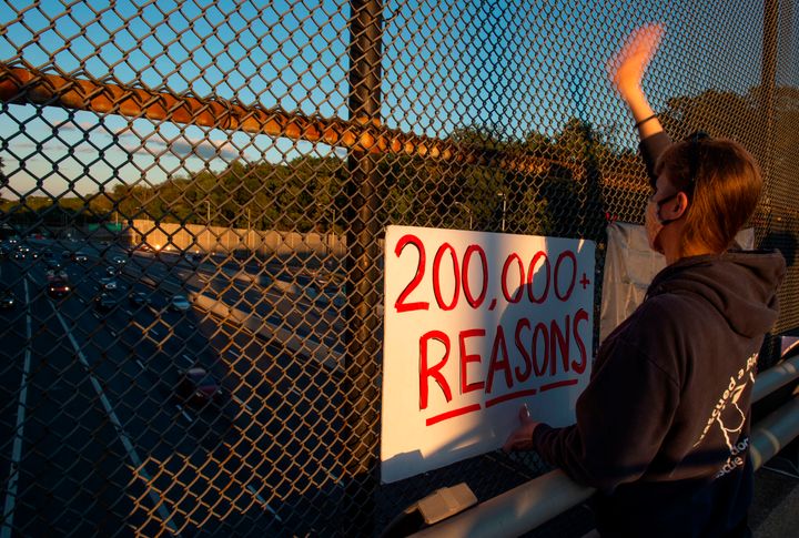 A supporter of Democratic Presidential candidate Joe Biden holds up a sign indicating the number of coronavirus deaths in the United States over a freeway in Arlington, Virginia on October 2.