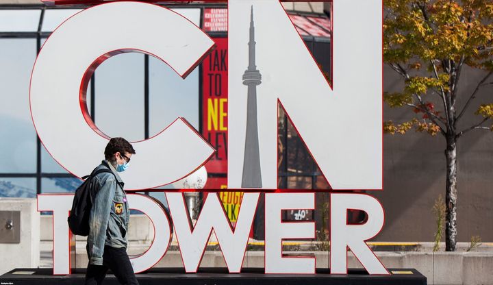 A man wearing a face mask walks past the CN Tower's sign in Toronto, Oct. 3, 2020. Canada's economic recovery appears to be running out of steam amid a second wave of COVID-19, CIBC says.