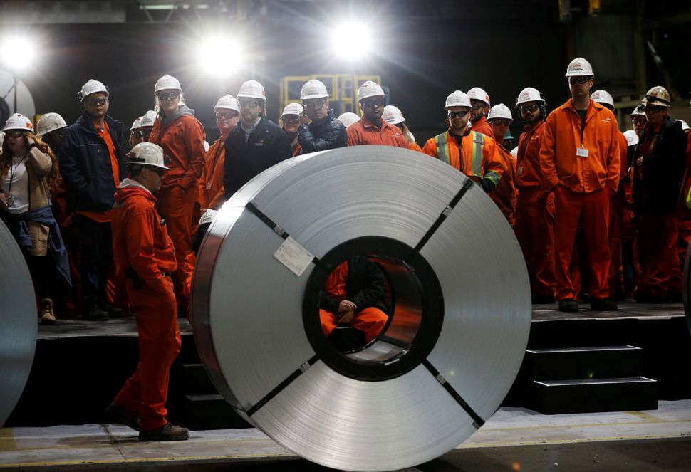 Workers stand behind rolls of steel at the ArcelorMittal Dofasco steel plant in Hamilton, Ontario, Canada, March 13, 2018. REUTERS/Mark Blinch TPX IMAGES OF THE DAY