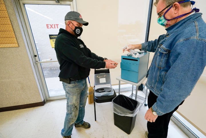 Chris Helps, of Earlham, Iowa, gets his hands sanitized by polling place volunteer Frank Hayer, right, during early voting, T