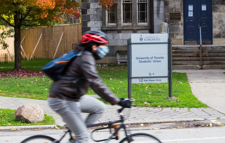 A woman wearing a face mask rides a bicycle past the Students' Union building at the University of Toronto in Toronto, Canada, on Oct. 20, 2020.