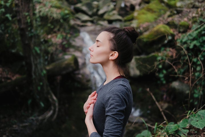 Young woman practicing breathing yoga pranayama outdoors in moss forest on background of waterfall. Unity with nature concept