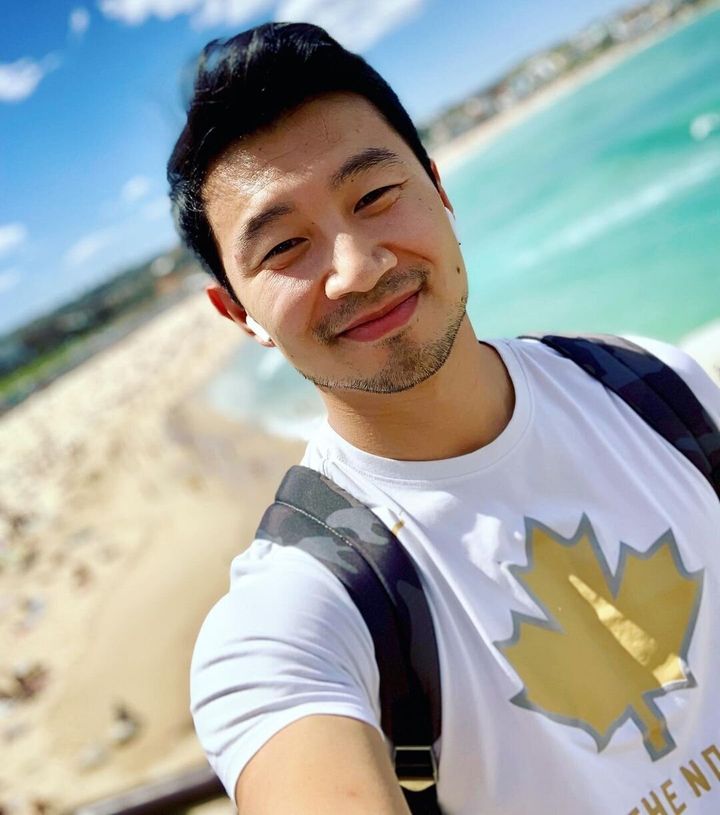 Simu Liu, pictured in a beautiful Australian climate and wearing a shirt repping Canada, is offering his emotional support to anxious Americans.