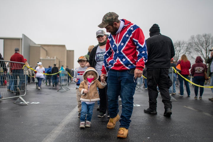 A man wearing a Confederate flag-themed sweatshirt walks with his children while queuing before President Donald Trump holds