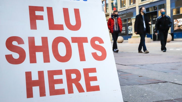 People wear masks as they pass a pharmacy offering flu shots in downtown Calgary, Alta., on Oct. 30, 2020.