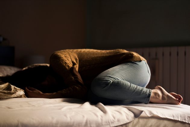 Une femme, en boule, dort sur son lit (photo