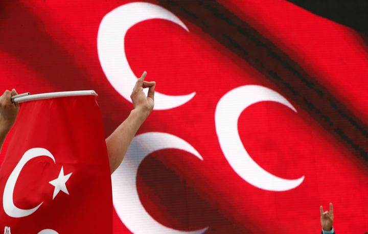 Τουρκική σημαία και το χέρι ενός άνδρα που σχηματίζει με τα δάχτυλά του το σύμβολο των Γκρίζων Λύκων. 