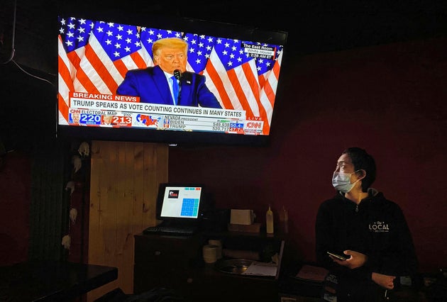 BEIJING, CHINA - NOVEMBER 4: A waitress wears a protective mask while watching a speech by the President of the United States ...