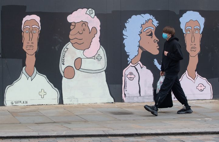 A man wearing a protective face mask passes a mural showing Black and Asian medical and transport workers, in Waterloo