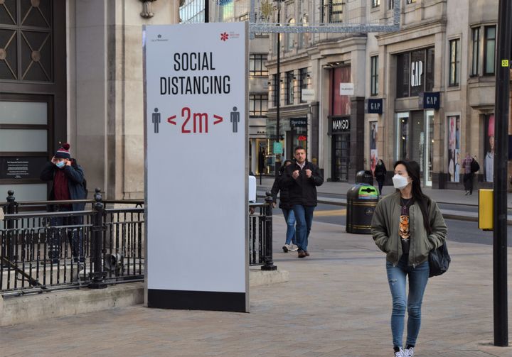 A woman wearing a face mask as a precaution walking past a social distancing sign on Oxford Street.