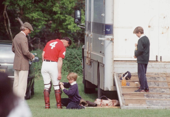 In a candid moment from 1993, a nine-year-old Prince Harry helps his dad with his polo boots.