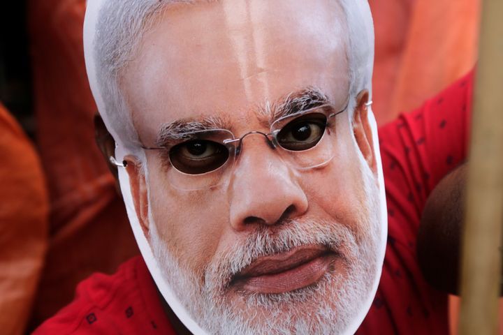 A supporter of India's ruling Bharatiya Janata Party (BJP) looks through a mask of Indian Prime Minister Narendra Modi during a protest rally allegedly against atrocities of police and Trinamool Congress party on BJP supporters in West Bengal state in Kolkata, India, Wednesday, June 12, 2019. (AP Photo/Bikas Das)