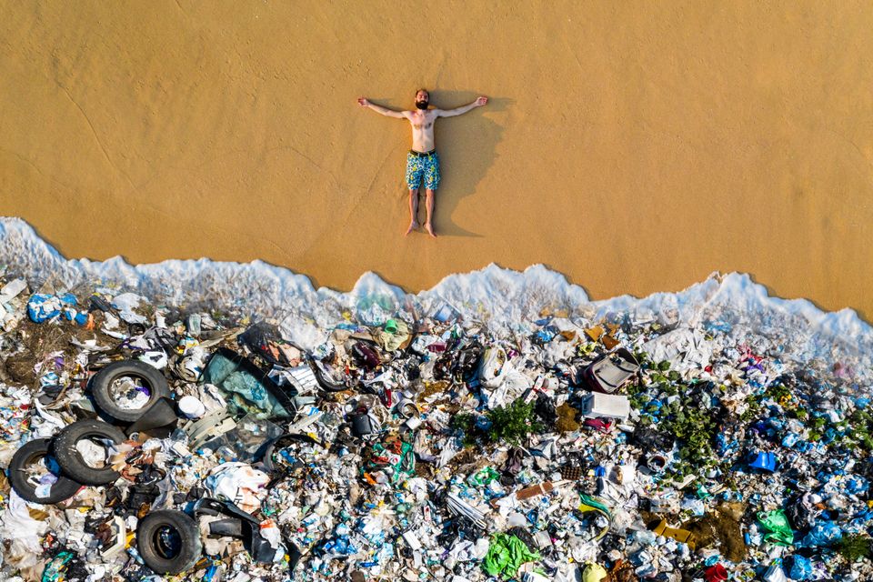 A man lying on the beach covered in trash