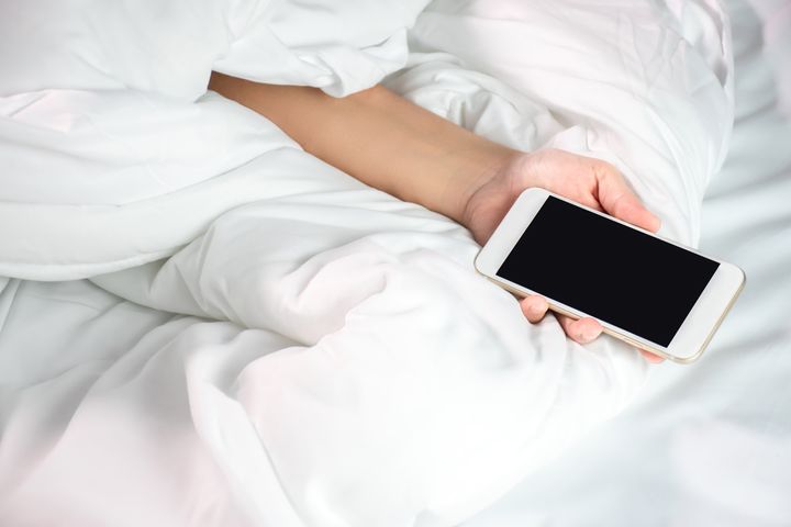 A woman lying in bed and holding a smartphone.