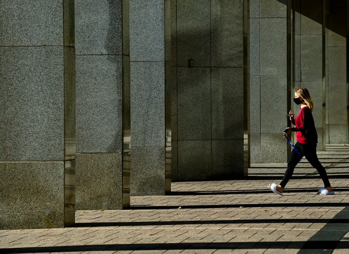A woman wears a mask as rays of light shine through building columns on a cool sunny fall morning in Toronto on Nov. 2, 2020.