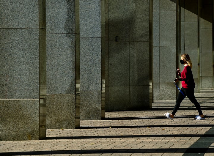 A woman wears a mask as rays of light shine through building columns on a cool sunny fall morning in Toronto on Nov. 2, 2020. 