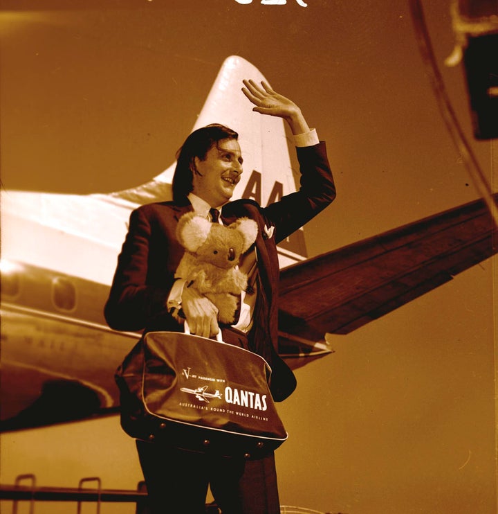 Australian entertainer Barry Humphries holding koala bear and Qantas bag waving on arrival in Melbourne, September 1965.