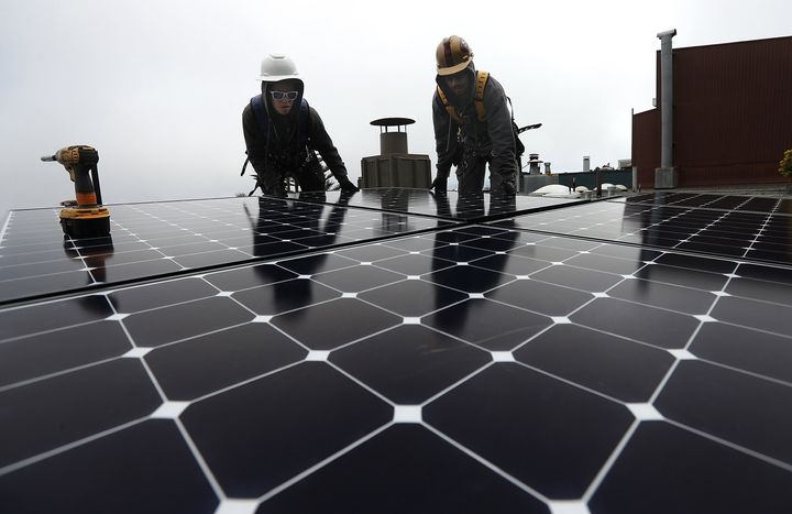 Luminalt solar installers Pam Quan and Walter Morales install solar panels on the roof of a home in San Francisco.