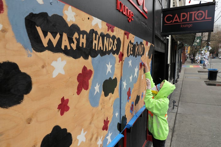 A woman works on a mural that reads "wash hands, be kind" in Seattle amid the coronavirus pandemic. Hundreds of miles away, a large recent wedding southwest of Spokane, Washington, is believed to have sparked COVID-19 outbreaks.