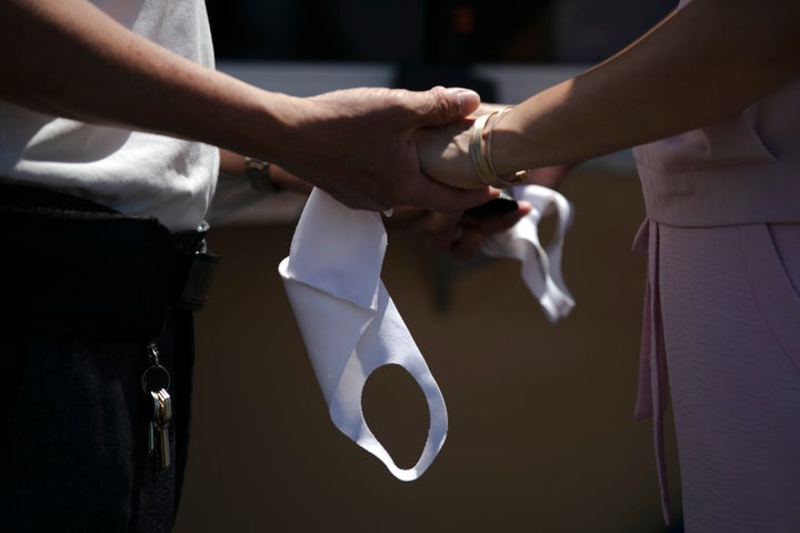 Una pareja se toma de las manos y máscaras mientras intercambian votos durante la ceremonia de su boda en un estacionamiento en Anaheim, California.