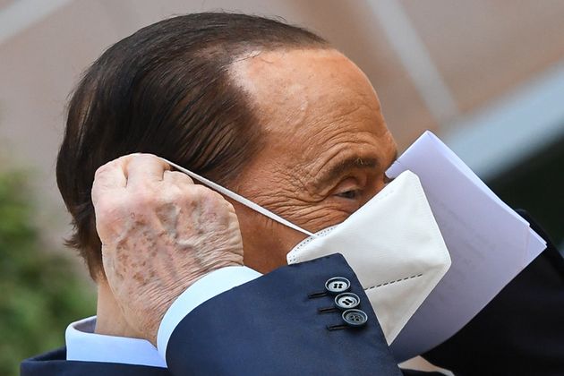 Former Italian Prime Minister Silvio Berlusconi removes his mask as he prepares to address the media, ...