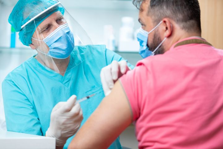 Doctor wearing protective visor and surgical gloves holding patient's arm to inject flu vaccine (file picture) 