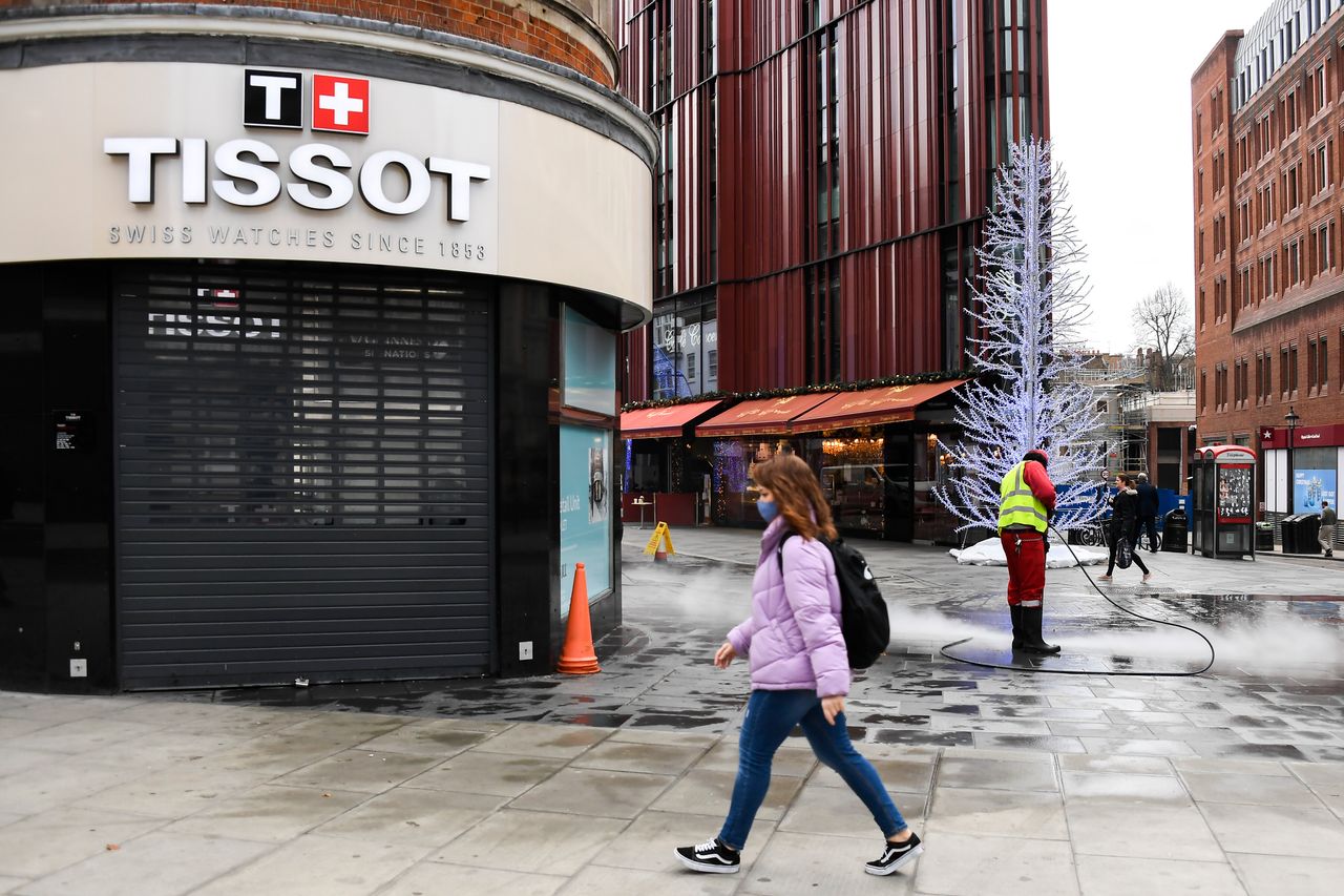 A woman walks past a closed shop while a man cleans the deserted pavement near Oxford Street in London on Tuesday. Oxford Street, one of Europe's busiest shopping zones, would usually be packed in the weeks before Christmas.